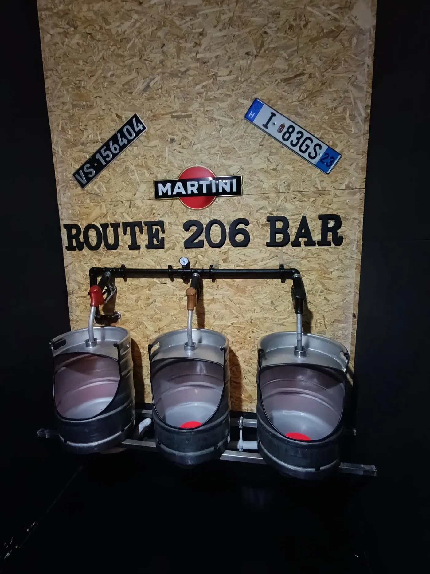 Três barris de cerveja ligados a pistolas de combustível, com o nome Route 206 Bar na parede