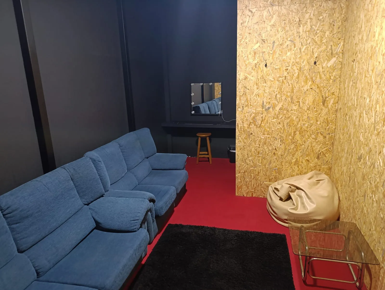 Camarim com sofá azul, espelho com lâmpadas e alcatifa vermelha