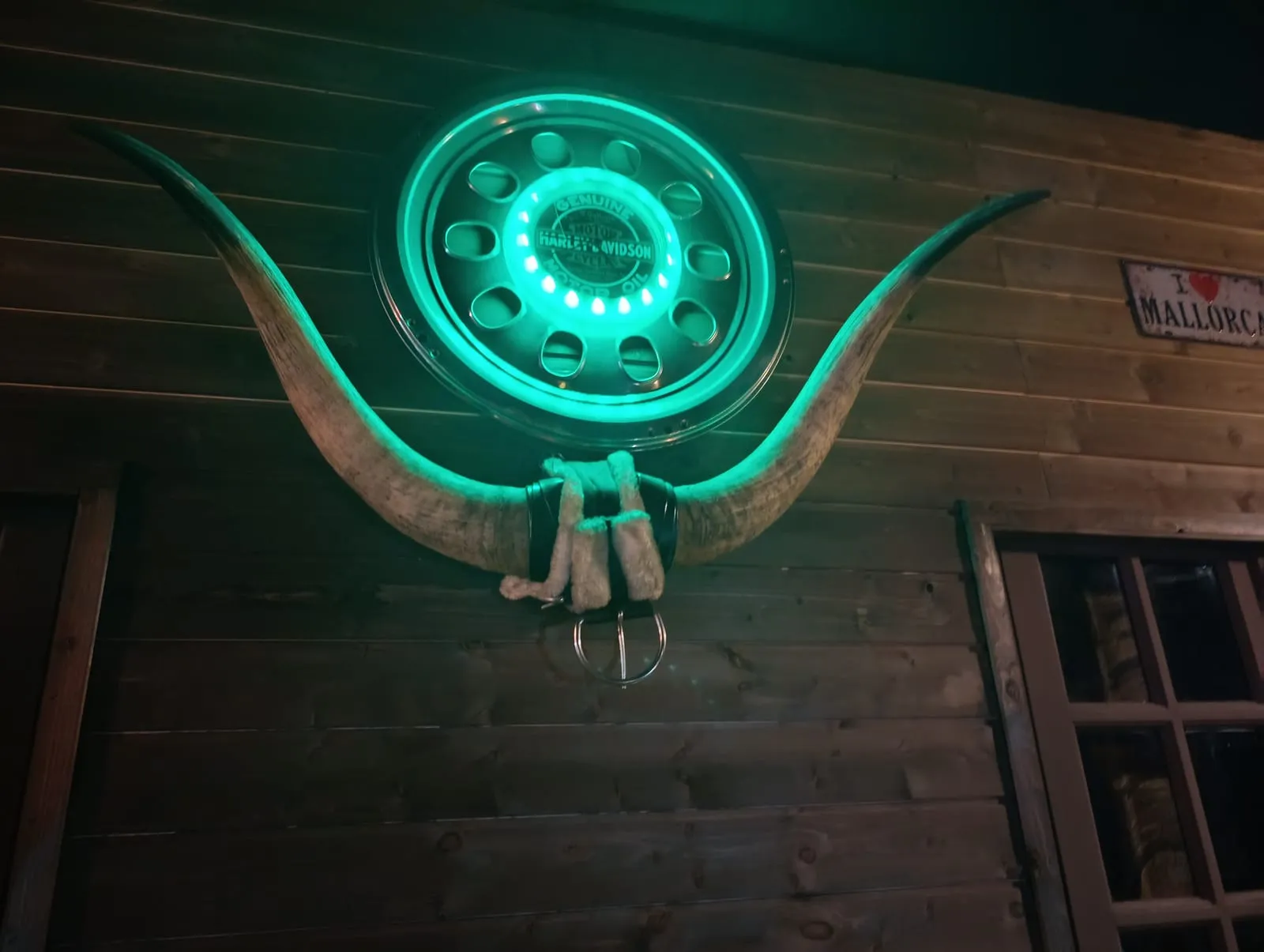 Chifres de touro na parede por baixo de uma jante Harley-Davidson iluminada a verde