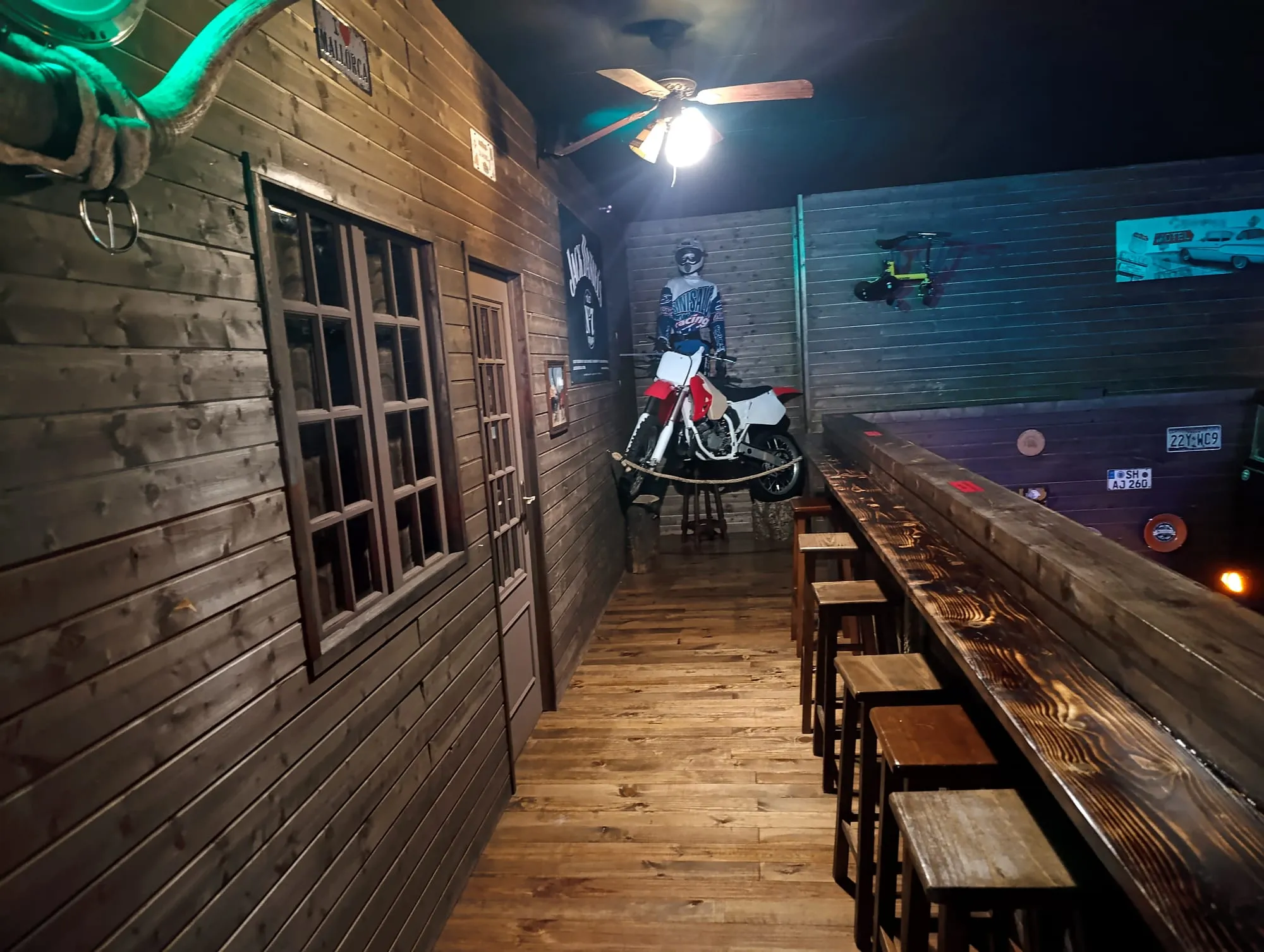 Corredor do bar com balcão corrido em madeira e uma mota de cross encostada ao fundo